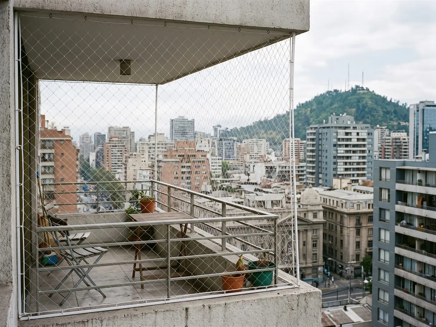 Balcón de una torre del centro de Santiago cerrado con malla de seguridad, con los edificios y un cerro al fondo