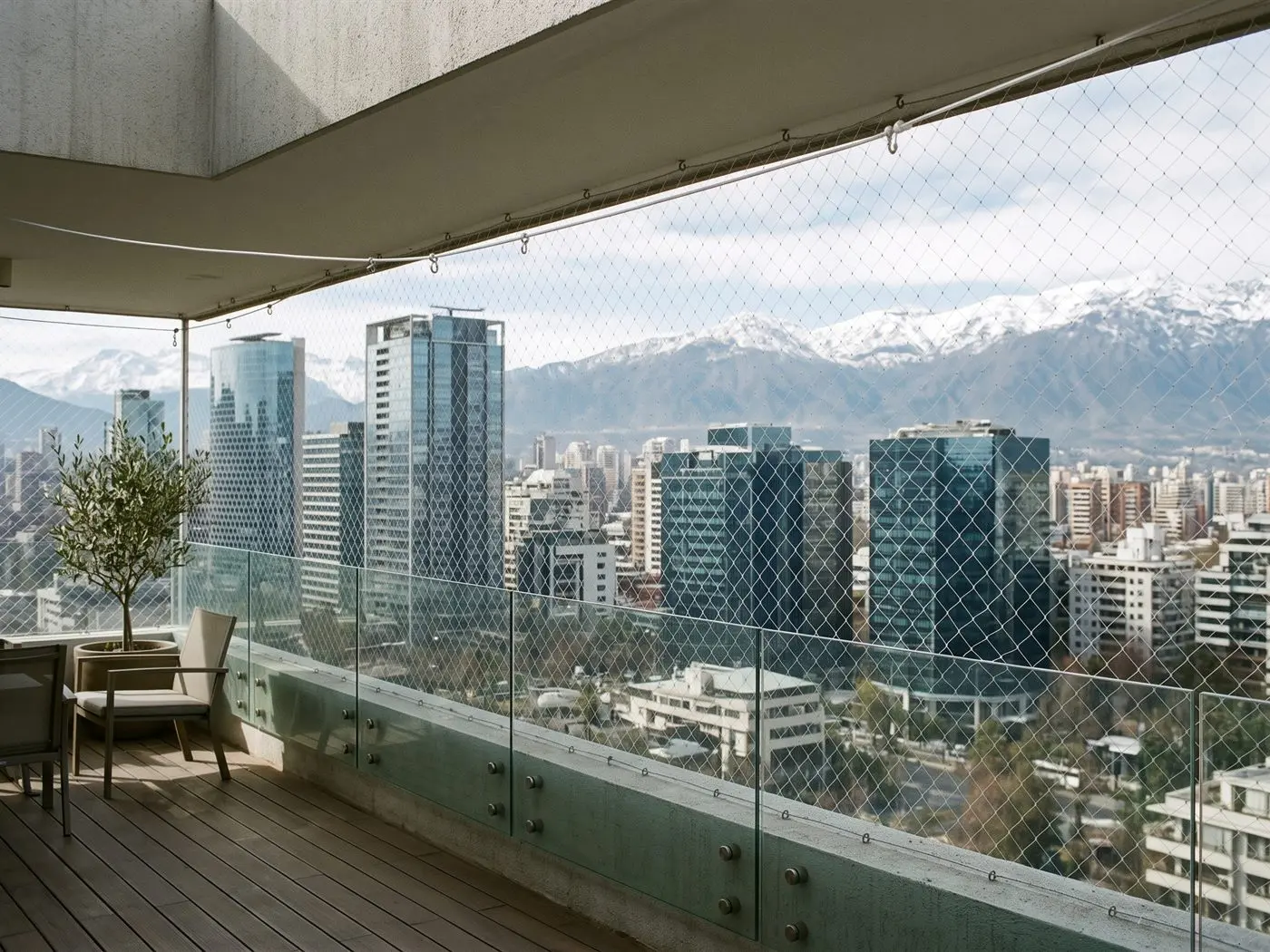 Terraza con baranda de vidrio de una torre de Las Condes cerrada con malla de seguridad, con las torres de oficinas y la cordillera