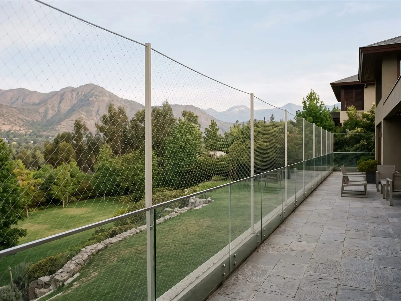 Terraza de una casa de Vitacura con baranda de vidrio y malla de seguridad vertical entre pilares, sobre el jardín