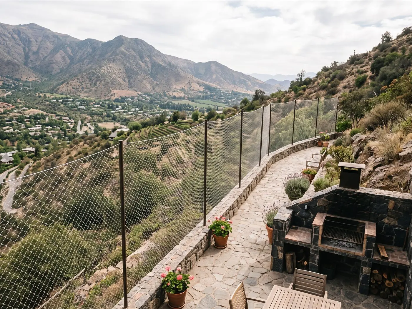Terraza de piedra en la ladera de una casa de Lo Barnechea con quincho y malla de seguridad entre pilares, con vista al valle