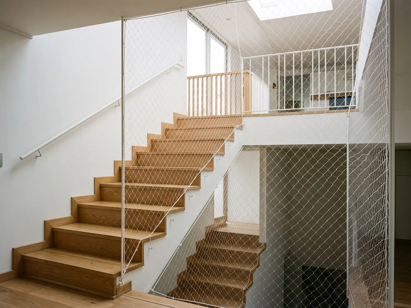 Escalera interior de madera con la malla de seguridad tensada en el lado abierto y en la baranda del segundo piso