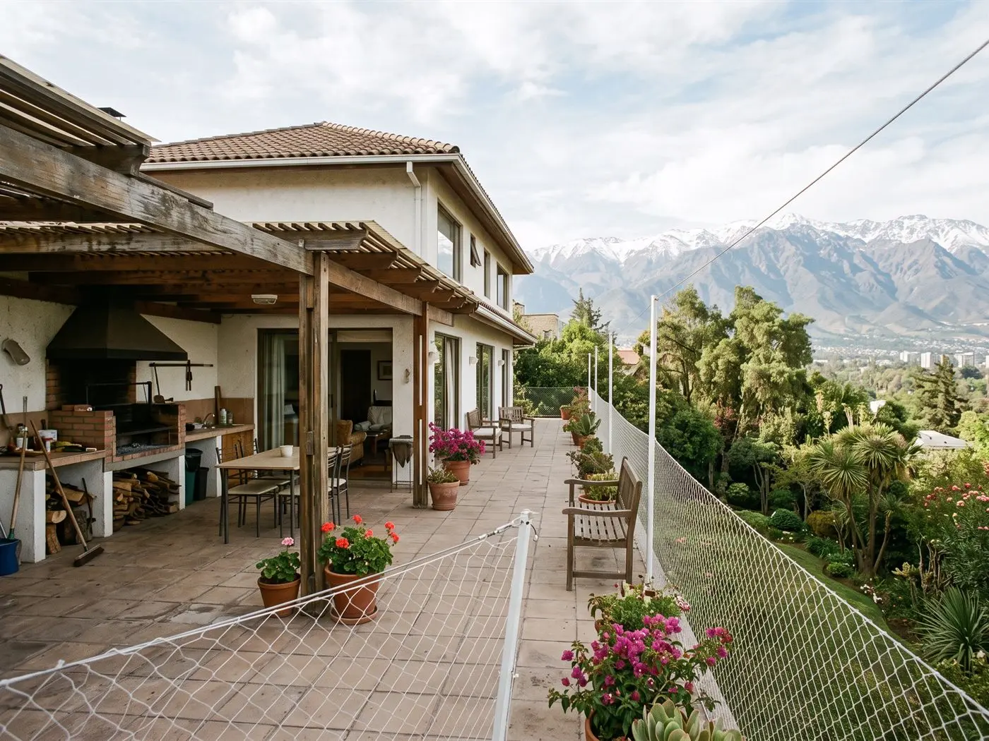 Terraza de casa con quincho cerrada con malla de seguridad sostenida por pilares, con el jardín y la cordillera detrás
