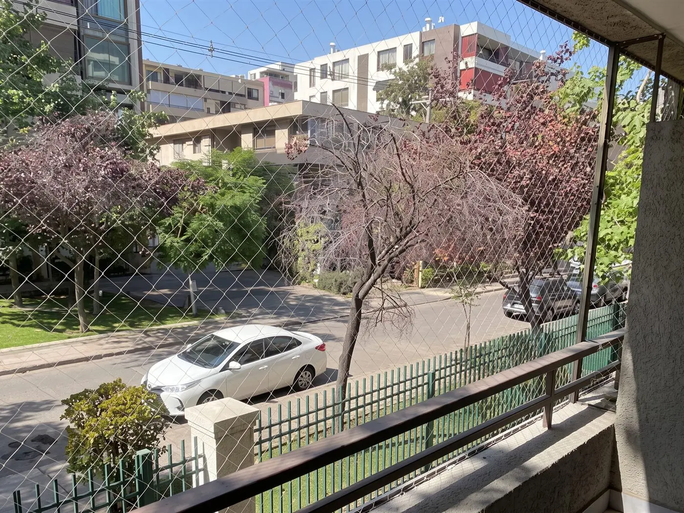 Malla de seguridad en un balcón de segundo piso frente a una calle arbolada, con la baranda y la reja del edificio