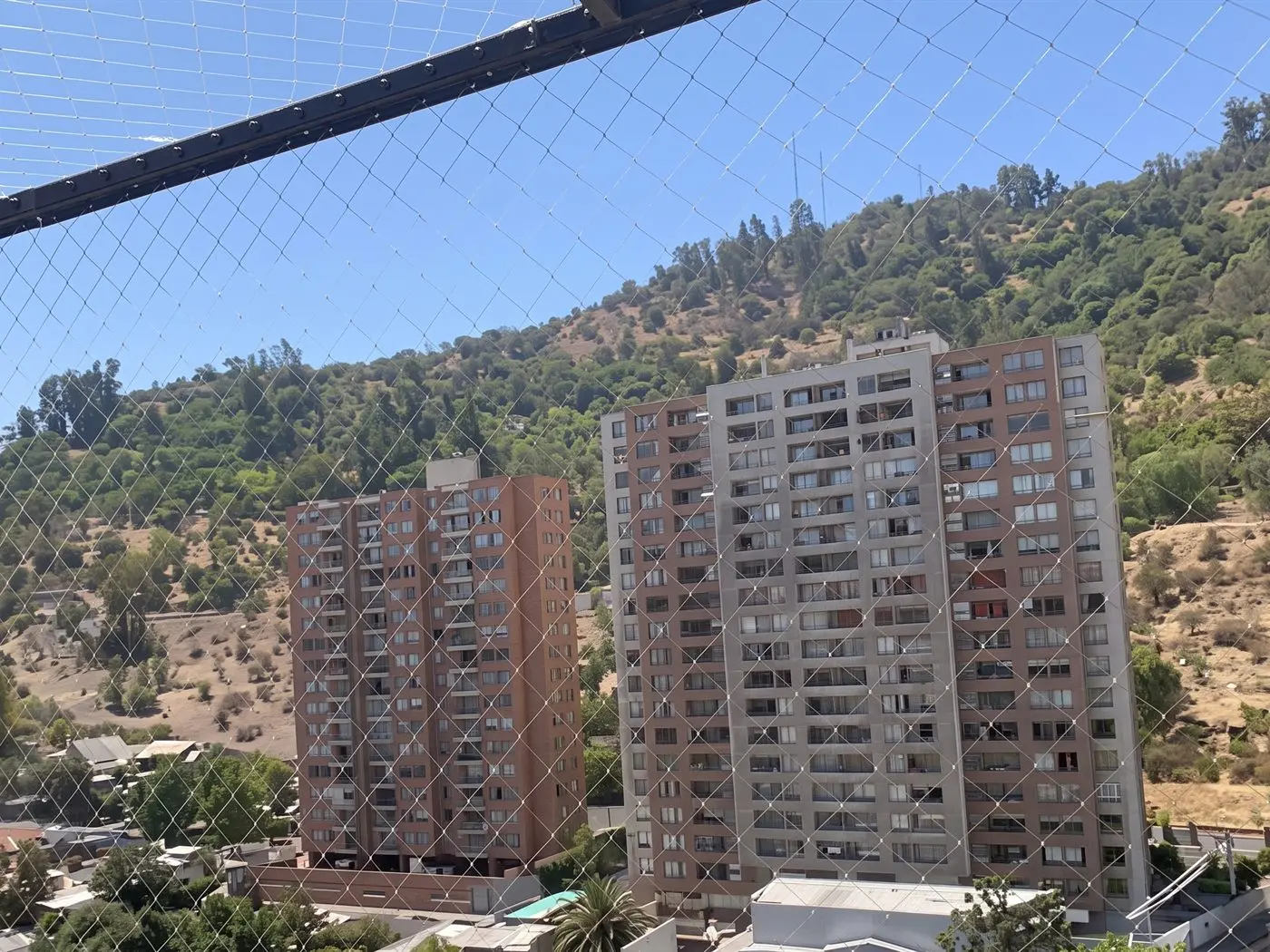 Malla de seguridad en el balcón de una torre, con el cerro y dos edificios de departamentos al fondo