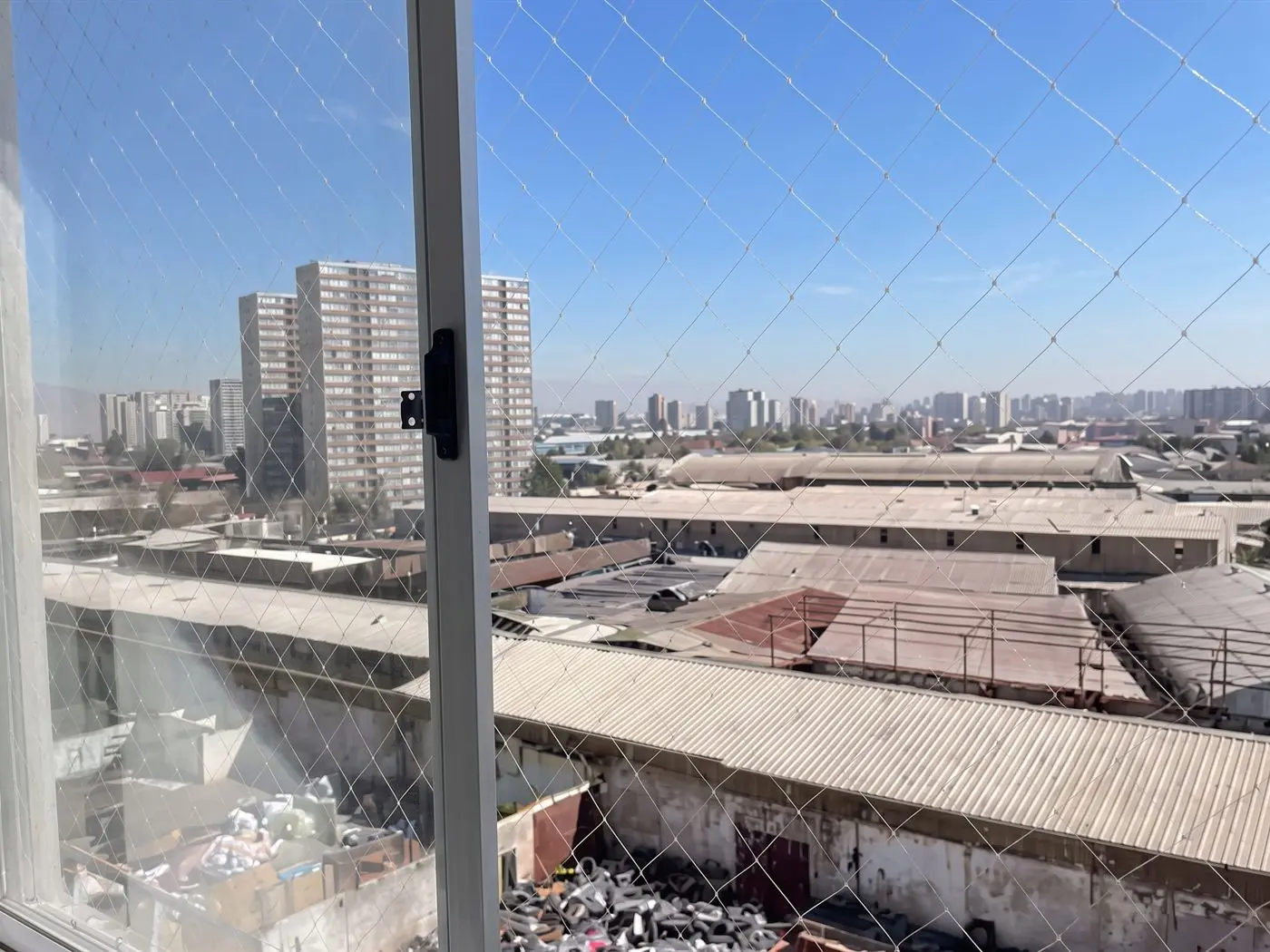Malla de seguridad instalada por fuera de una ventana corredera de aluminio, vista desde una pieza vacía